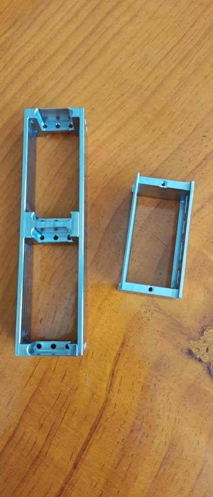 Two blue rectangular machined frames with open pockets and mounting holes